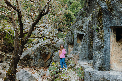 Side View of female traveler in pink sweatshirt walking in the mountains contemplating views of ancient world of Pinara in Lycia, South Turkey