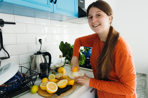 Female in orange shirt making tasty juice from fresh-gathered citruses in the white-blue authentic kitchen in Mediterranean Turkey