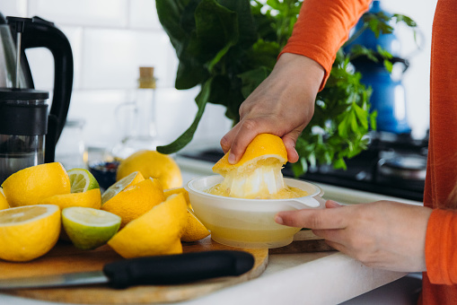 Female in orange shirt making tasty juice from fresh-gathered citruses in the white-blue authentic kitchen in Mediterranean Turkey