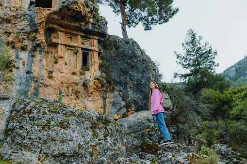 Side View of female traveler in pink sweatshirt walking in the mountains contemplating views of ancient world of Pinara in Lycia, South Turkey