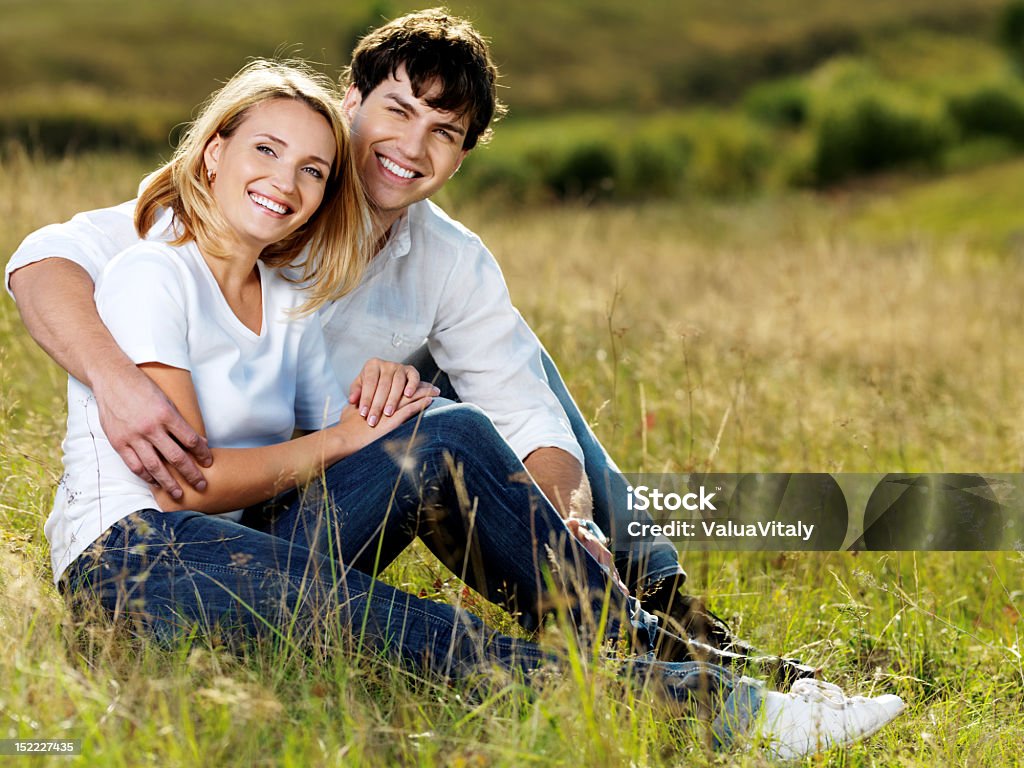 beautiful couple sitting in meadow young happy beautiful couple sitting in green meadow Adult Stock Photo