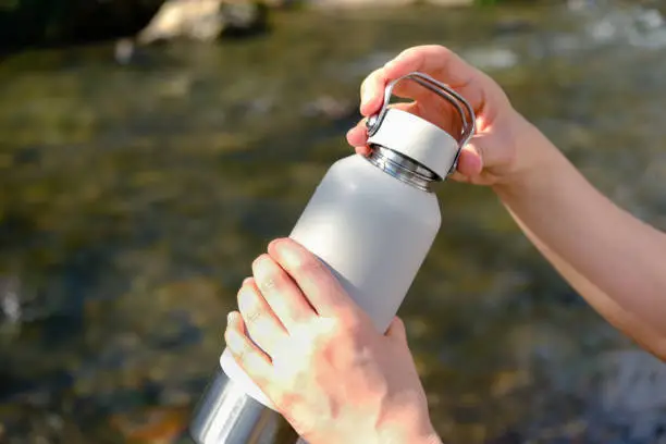 Closeup, Womans hands hold insulated reusable water bottle instead of single use plastic cup, open lid to drink her water. Eco friendly, zero waste and green living lifestyle.