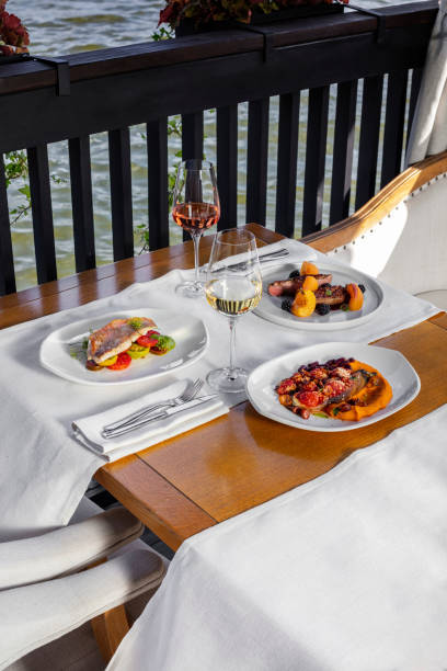 istock Three-course dinner with white wine. Eggplant with tomatoes, sea bass with vegetables and duck steak in blackberry sauce are on a wooden table. Nearby is a glass of white wine. 1522290117