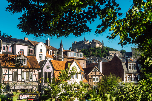 Street with historic buildings and a stream on the outskirts of Falaise. Saint-Laurent church on a hill in the background