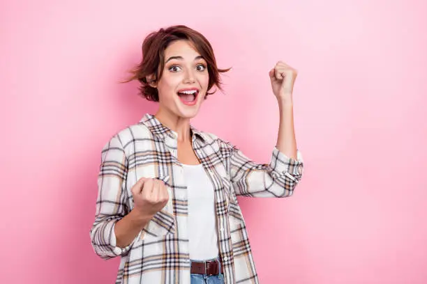 Photo of Photo of young successful business lady fists up lucky startup invention make project popular winner isolated on pink color background