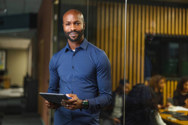 Portrait Successful African American Male Business Manager And Financial Advisor Waist up portrait of an attractive young Black businessman working with digital tools and online documents. He is smiling and looking at the camera. black man stock pictures, royalty-free photos & images