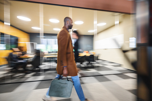Side view of an attractive African American male walking in a corporate office. He is carrying a briefcase and wearing casual clothing.
