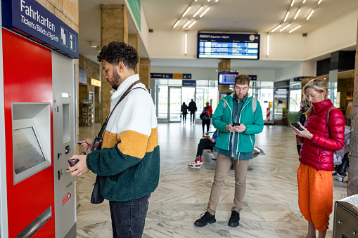 A side view of a same sex couple who are travelling Europe and are visiting Garmisch in Germany.They are in the towns train station and are paying for their onward travel using the contactless and cashless ticket machines.