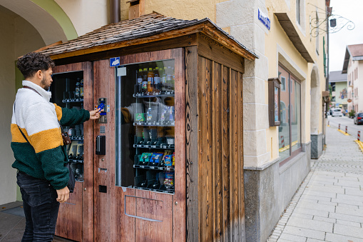 A medium close up over the shoulder view of a man who is travelling in Southern Germany in Garmisch. He is buying some local produce from the vending machine which allows local to spelt their products via the machines.