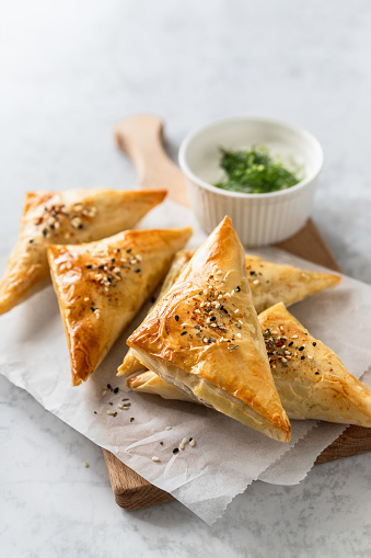 Cheese stuffed triangle filo pastry savory pies served with yoghurt sauce over baking paper on wooden board