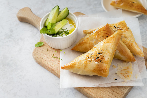 Filo pastry stuffed hand pies served with yoghurt tzatziki sauce on wooden board