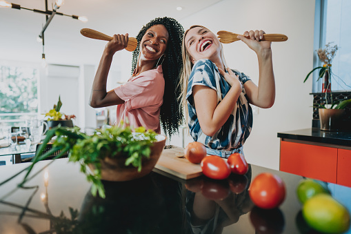 Two female friends singing while preparing food in the kitchen at home