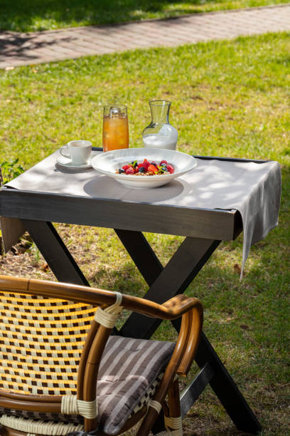 istock Breakfast granola with raspberries, strawberries and blueberries in a deep plate with wide margins. Nearby is a glass of juice and a carafe of yogurt. The food is on a wooden table in the middle of a clearing with a lawn. 1522424375