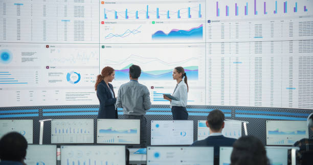 istock Wide Back Shot of Diverse Team of Data Scientists Discussing Graphs And Reports On Big Digital Screen In Monitoring Office. Multiethnic Employees Working On Desktop Computers For Deep Learning Company 1522425251