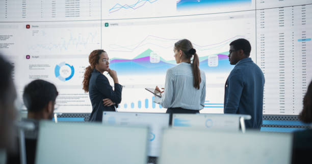 istock Diverse Team Of Data Scientists Having A Meeting And Discussing Reports In a Modern Monitoring Office With Analytics Feed On a Big Digital Screen. Deep Learning Company With Employees Behind Computers 1522425438