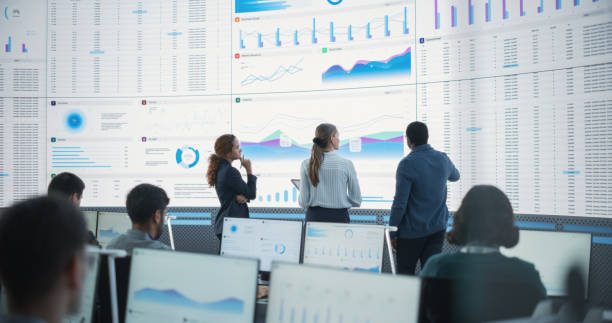 istock Diverse Team Of Data Scientists Having A Meeting And Discussing Reports In a Modern Monitoring Office With Analytics Feed On a Big Digital Screen. Big Data Company With Employees Behind Computers 1522425611