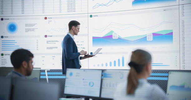 istock Male Senior Financial Analyst Reviewing Information And Reports on Big Digital Screen in Modern Monitoring Office. Diverse Employees Working Behind Desktop Computers In Investment Management Company. 1522425794