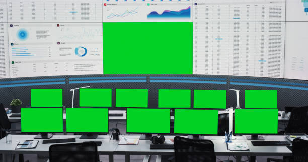 istock Empty Modern Monitoring Office With Green Screen Chromakey On Big Digital Screen And Desktop Computer Monitors Of Employees. Mockup Template Of Successful AI Or Deep Learning Company Workspace. 1522426177