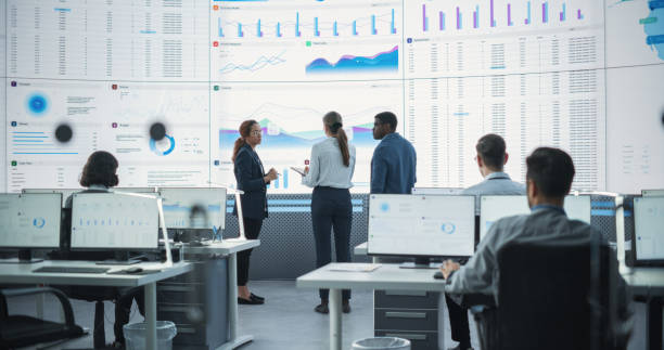 istock Diverse Team Of Data Scientists Analyzing Information And Graphs On Big Digital Screen In Modern Monitoring Office. Multiethnic Employees Working Infront Of Desktop Computers In Consulting Firm. 1522426414