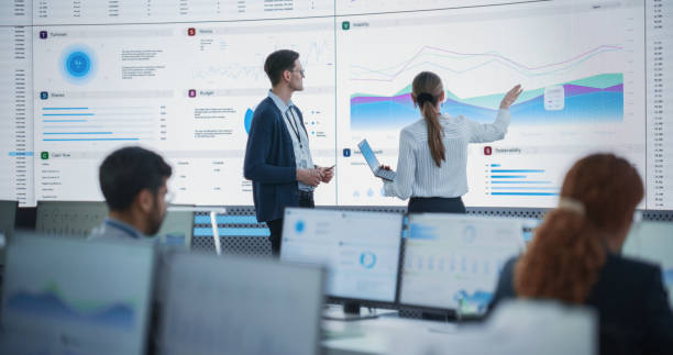 istock Female Data Scientist And Male Project Manager Discussing Reports And Graphs On Big Digital Screen In Monitoring Office. Diverse Employees Working Behind Computers in Artificial Intelligence Company. 1522427440