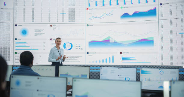istock Caucasian Female Data Scientist With Tablet Computer Is Reviewing Reports Of Diverse Employees on Big Digital Screen In Monitoring Room. Team Of Analysts Listening To New Objectives And Tasks. 1522429186