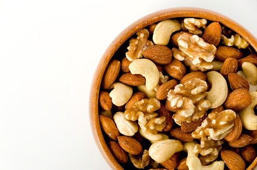 mix of nuts in a wooden bowl on a white background.