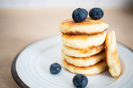 Appetizing homemade syrniki (cottage cheese pancakes), with blueberries on a plate in the kitchen. Close-up, mockup. Traditional cuisine. A delicious and nutritious sweet breakfast