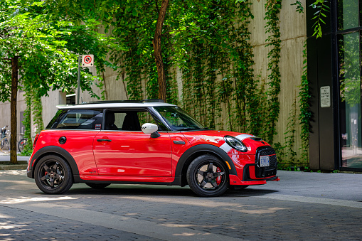 Toronto, Ontario, Canada- July 1, 2023. Chili red colour MINI COOPER on the urban street  in downtown Toronto East side, Canada. Evening in spring time. This is the third generation model F56 JCW, since BMW took over iconic brand of MINI. MINI featured in the photo is John Cooper Works model, the most powerful 2 door version. This compact car features engine build and designed by BMW, and packs even more power and torque than previous models, since 2002 to present. Original design clues and themes are still present on this brand new model. Mini has been around since 1959 and has been owned and issued by various car manufacturers.