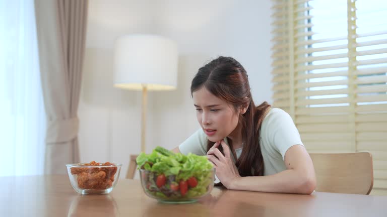 Asian woman deciding whether to choose a healthy vegetable salad or opt for unhealthy fried food.