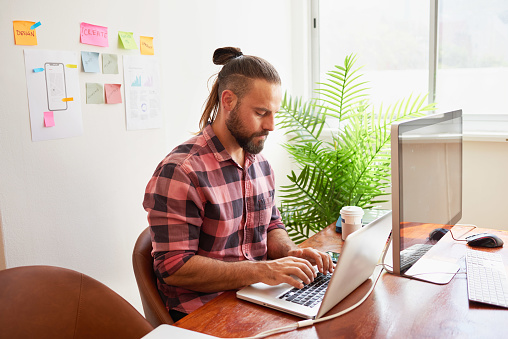 Senior developer works in open plan creative office, man bun hipster look. High quality photo