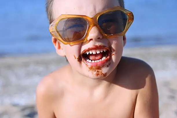 Boy in the sun glasses, soiled by chocolate. Beach.