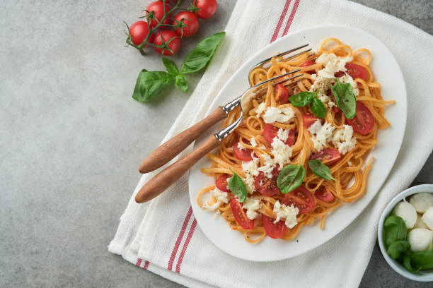 istock Salad caprese or pasta spaghetti broken with basil and mozzarella ala caprese on white plate on grey rustic concrete background. Traditional Italian cuisine. Italian food concept.  Top view. Recipe. 1522595852