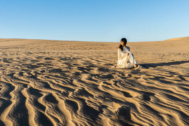 A woman dressed in white is watching the sunset on a dune