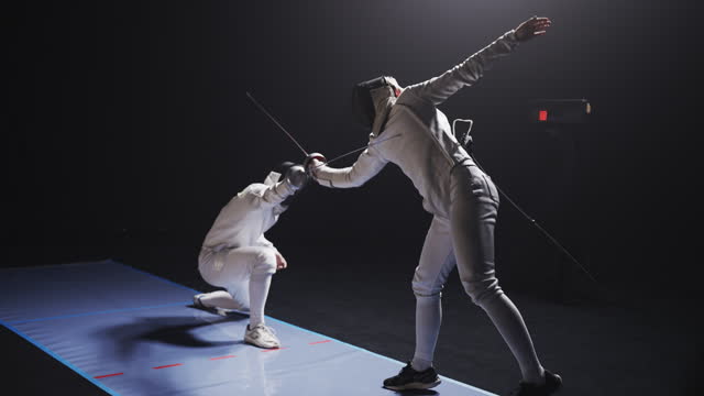 Rear view two professional fencers in full protective gear clashing foil sabers in a match. Ducking low and parrying