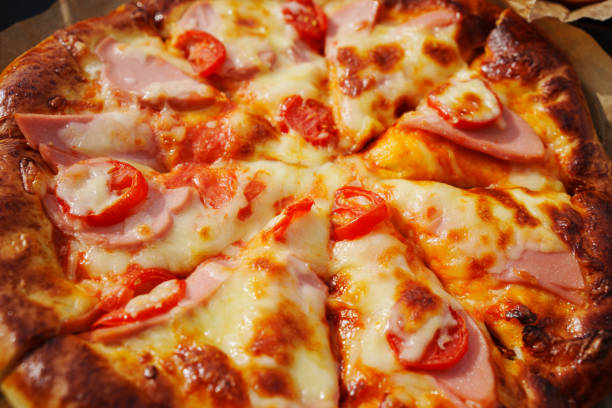 close-up. Pizza with ham, cheese and tomatoes. A delicious and simple Italian party dish. Ordering and delivery of food from a cafe and restaurant to your home.