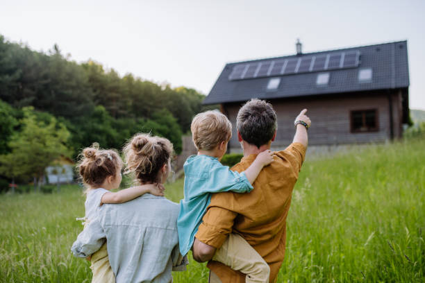 Happy family in front of their house with solar panels on the roof. stock photo