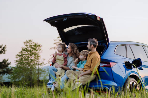 Happy family sitting in a car trunk and waiting for charging. stock photo