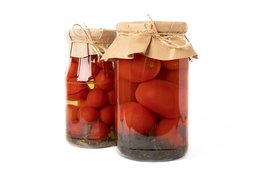 Pickled red cherry tomatoes in a glass jar isolated on white background. Food preservation for autumn or winter. Home storage. Canning, fermentation concept. Place for text. Copy space.