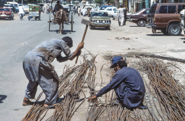 Peshawar, Pakistan - June 30, 1987: street worker prepare iron rods for forming a grid for plaster stabilization.