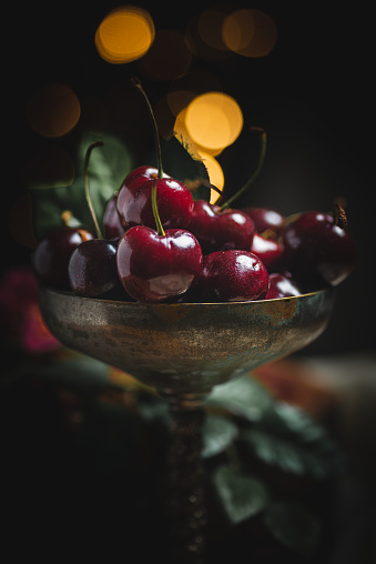 close-up of organic cherries, in an antique metal cup, on a table with a piece of cloth and dark background