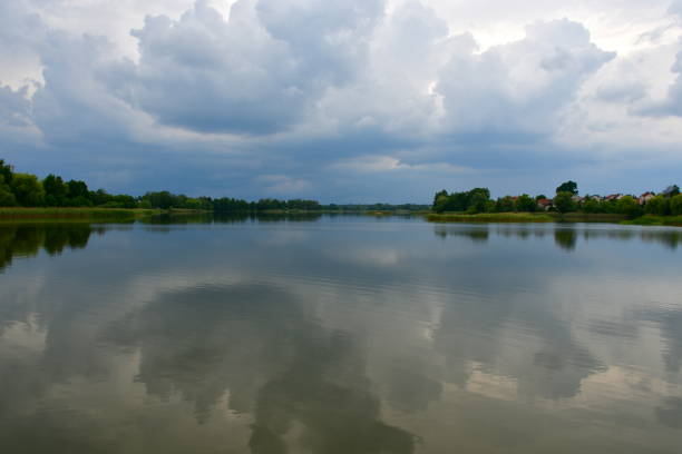 A close up on a vast yet shallow river surrounded from all sides with forests, moors, and small villages seen just before a massive thunderstorm and rainfall on a sunny summer day in Poland