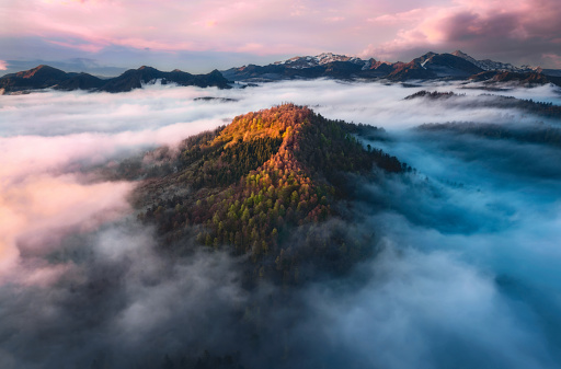 Aerial view of Mountain peak with sunlight and colorful forest in fog at sunset. Slovenia