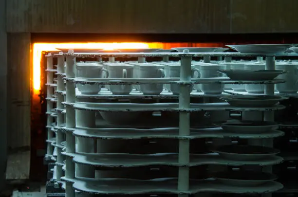 Photo of porcelain blanks of white plates on stands move along the container into a muffle furnace for firing