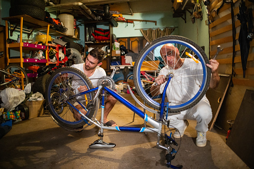 Dedicated Caucasian father and his son together repair bicycle at the messy garage