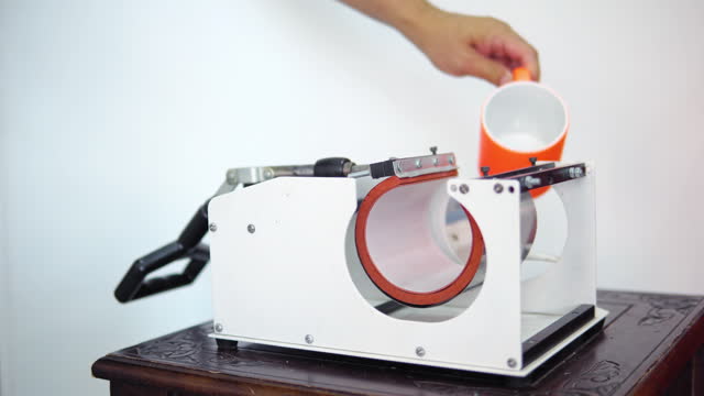 Man putting mug in a thermopress for cup print - intended for transfer image or a logo on a mug, cup