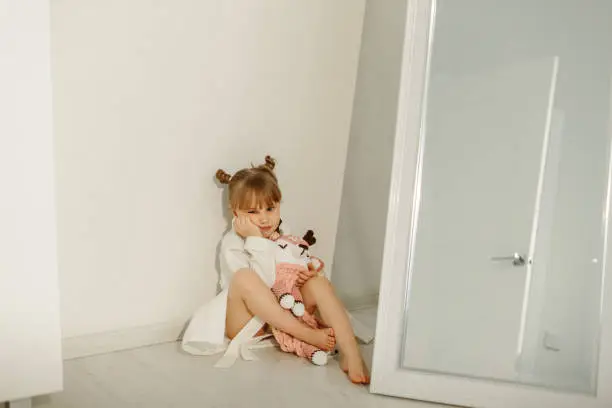 Photo of A girl in a bathrobe plays on the floor with a knitted unicorn