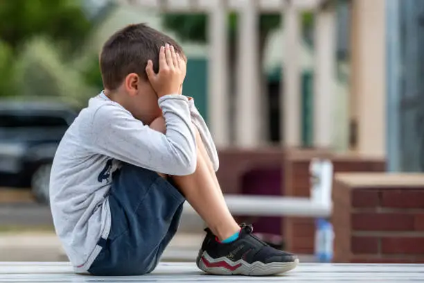 Photo of Crestfallen Crying child boy sitting at the schoolyard covering his face