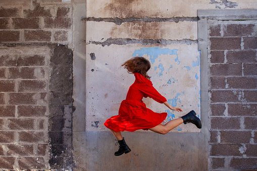 Young girl in a red dress and boots jumping in the air