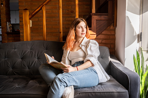 Young woman contemplating while hold a book at living room