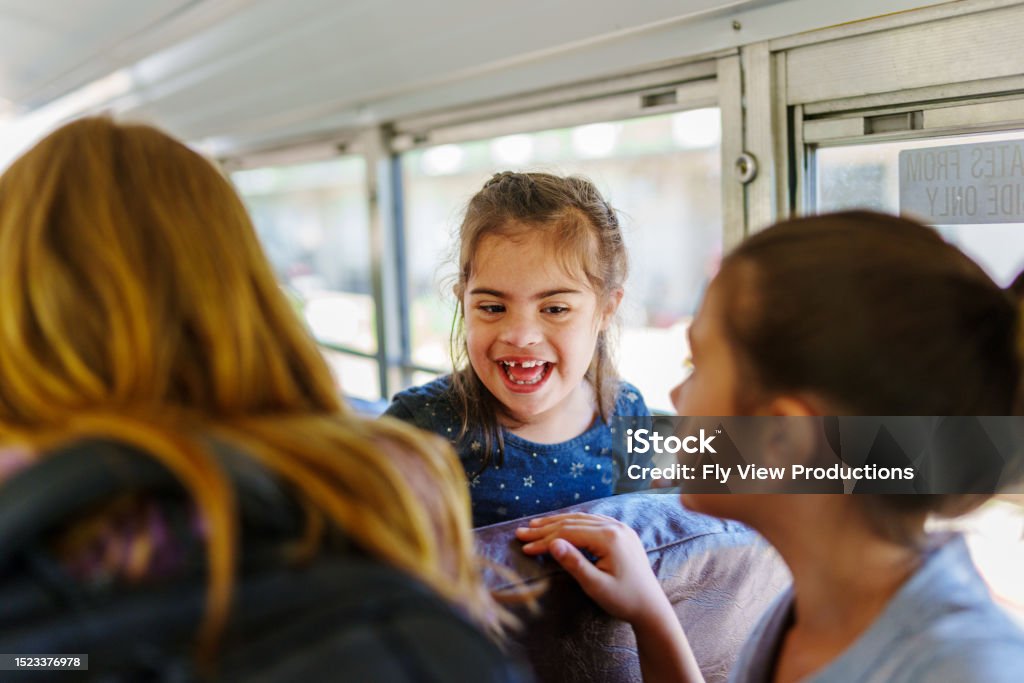 Happy friends talking together on school bus Three elementary age girls laugh and talk together while on a school bus. Selective focus on a Hispanic girl who has down syndrome. Child Stock Photo